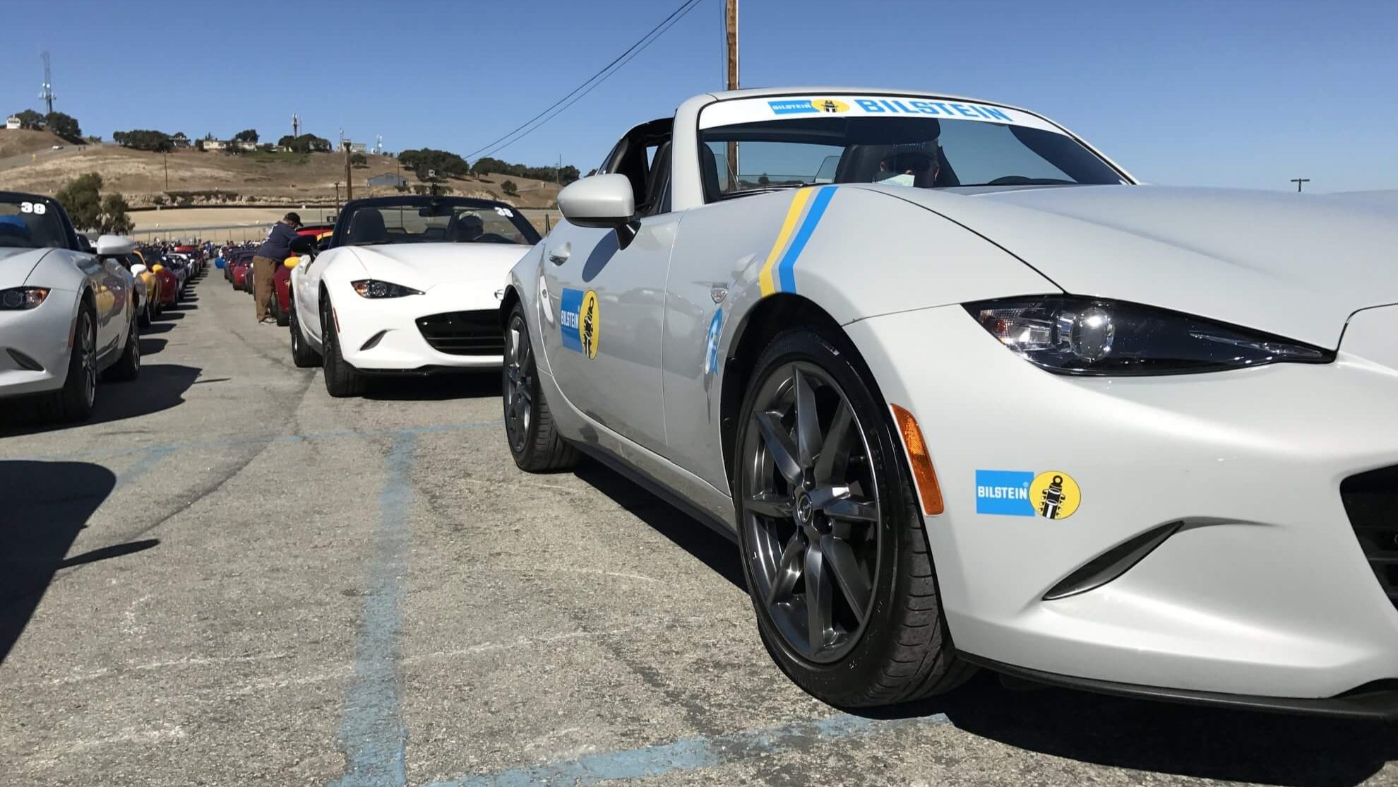 Row of sports cars ND Miata on a track with clear blue sky
